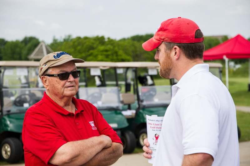 a man in a red shirt and cap talking to another man