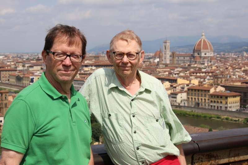 two men standing on a ledge with a city in the background