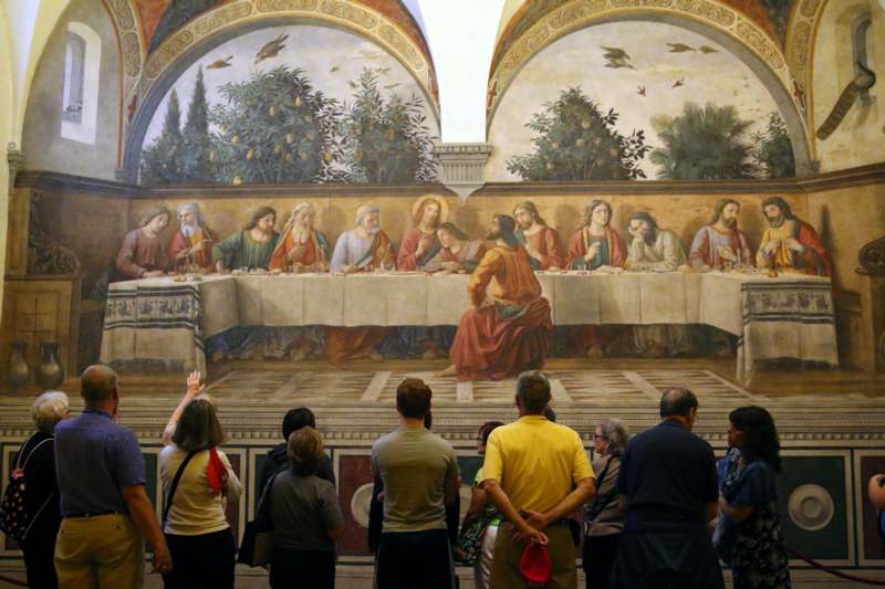 a group of people standing in a room with a painting on the wall