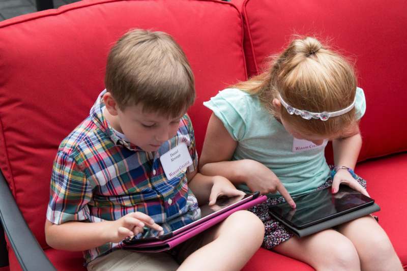 a boy and girl sitting on a couch using a tablet