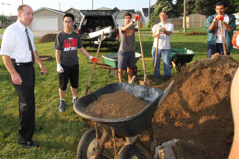 a group of people standing in a yard with a wheelbarrow and shovels