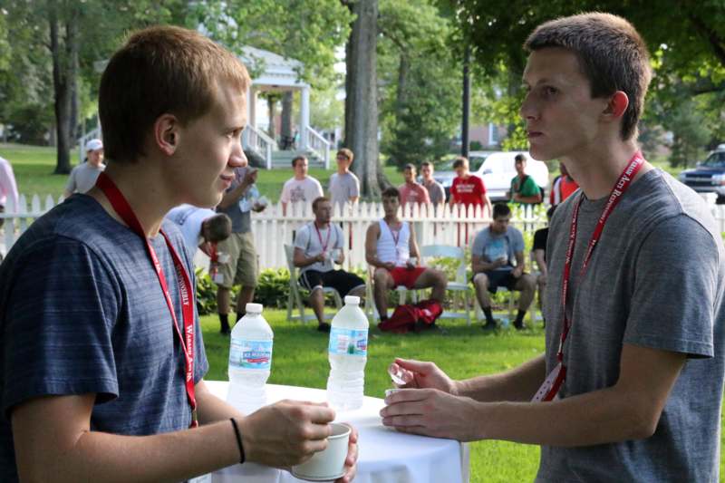 two men talking at a table with water bottles and a cup