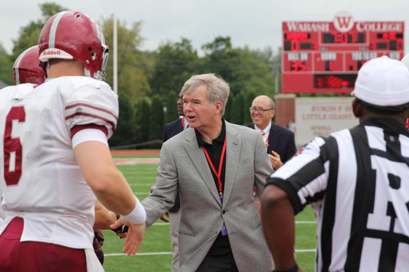 a man in a grey suit shaking hands with other men on a football field