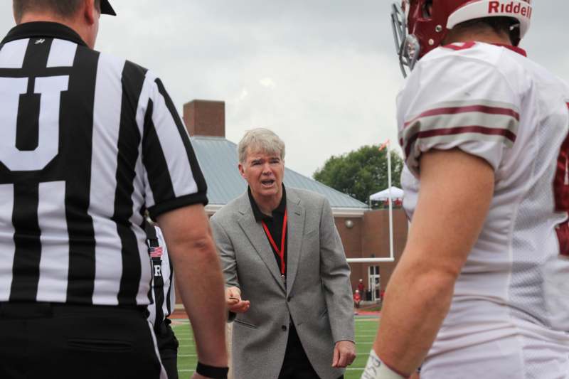 a man in a grey suit talking to a group of men on a football field