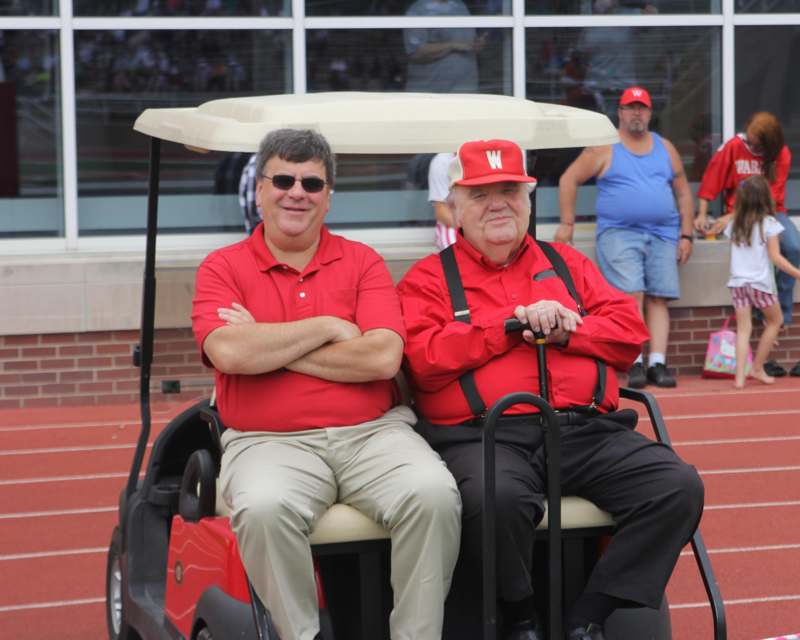 two men in red shirts sitting in a golf cart