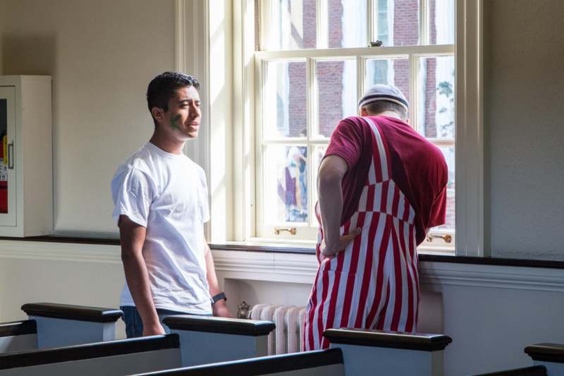 a man in a striped apron standing next to a man in a room with windows