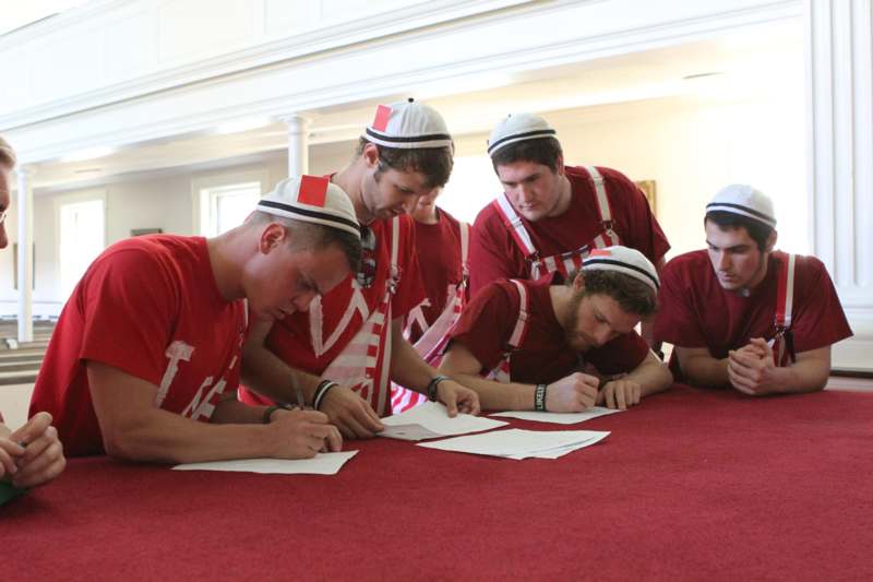 a group of men in red shirts and hats writing on paper