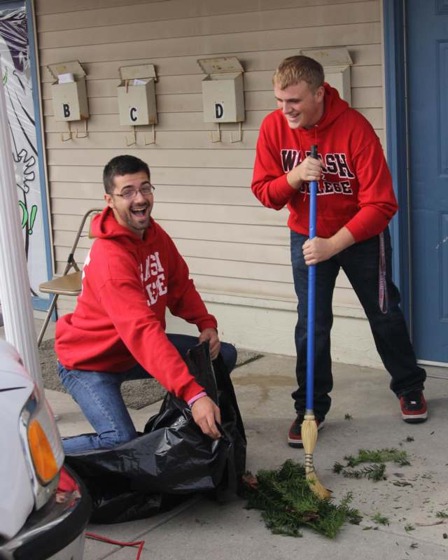 two men in red hoodies holding a broom and a bag