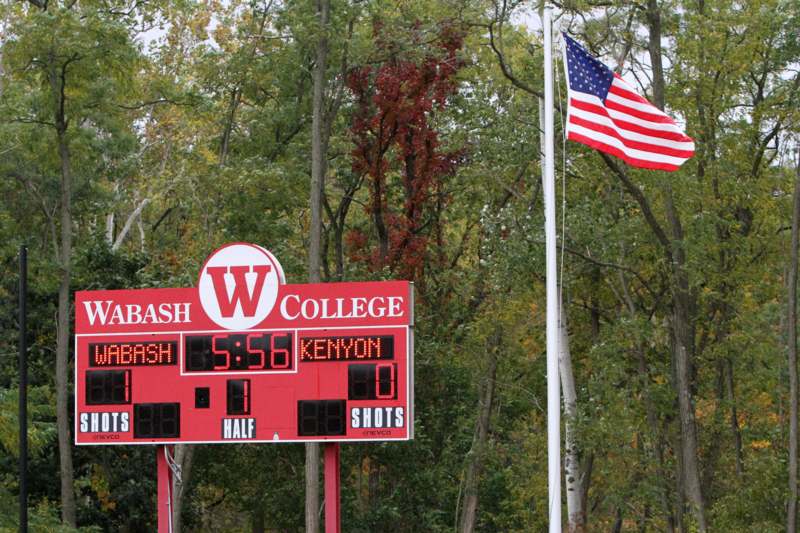 a scoreboard with a flag and a pole with trees in the background