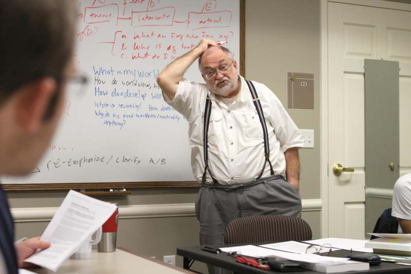 a man in suspenders standing in front of a whiteboard