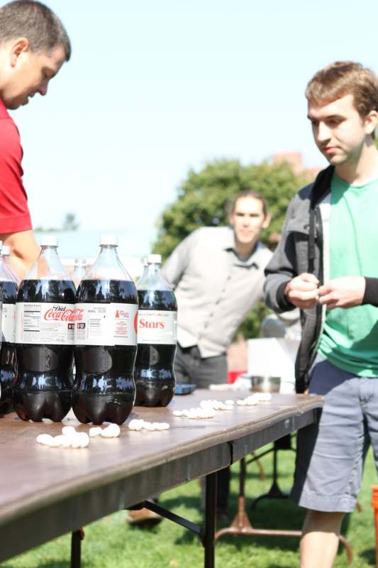 a group of men standing next to a table with bottles of soda