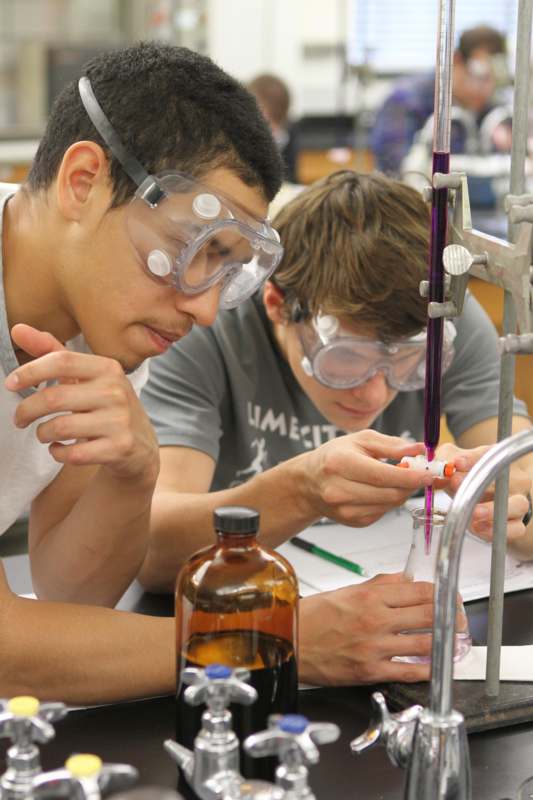 a pair of young men wearing safety goggles and looking at a test tube