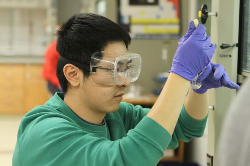 a man wearing protective goggles and gloves holding a test tube