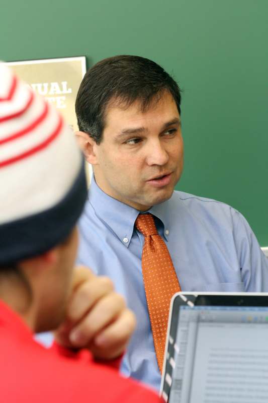 a man in a blue shirt and orange tie talking to a student