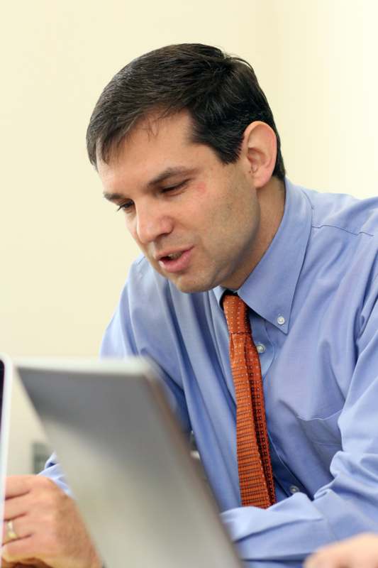 a man in a blue shirt and tie looking at a laptop