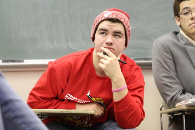 a man in a beanie and a red sweater with a pen in his hand