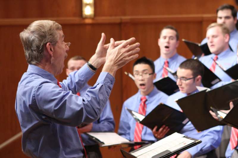 a man in a blue shirt with his hands up in front of a group of men singing