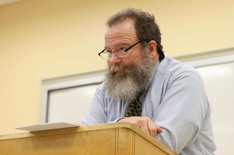 a man with a beard sitting at a podium