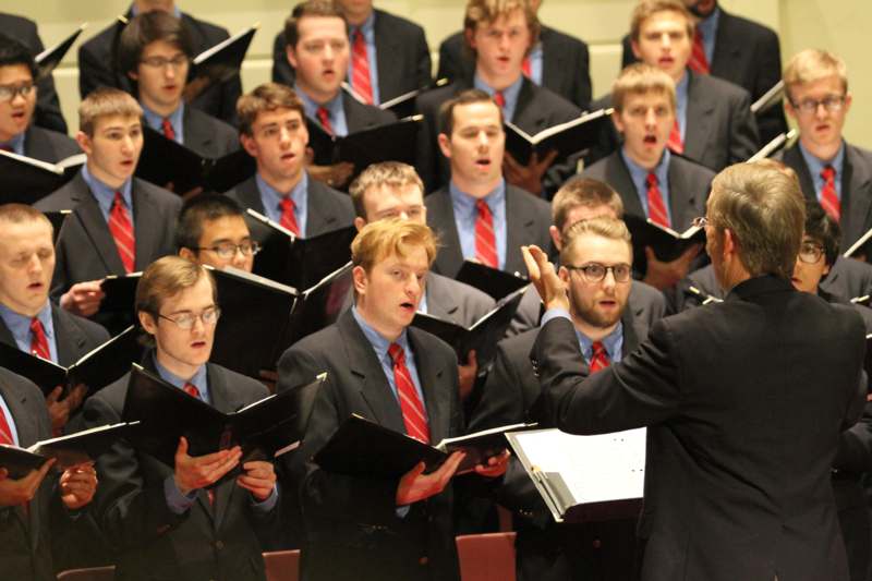a man in suit and tie singing into a choir