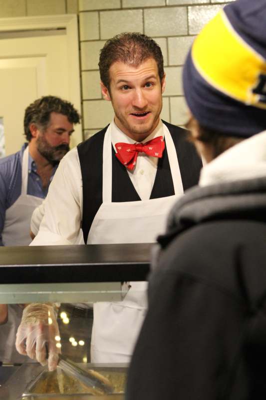 a man in apron and bow tie standing in front of a counter