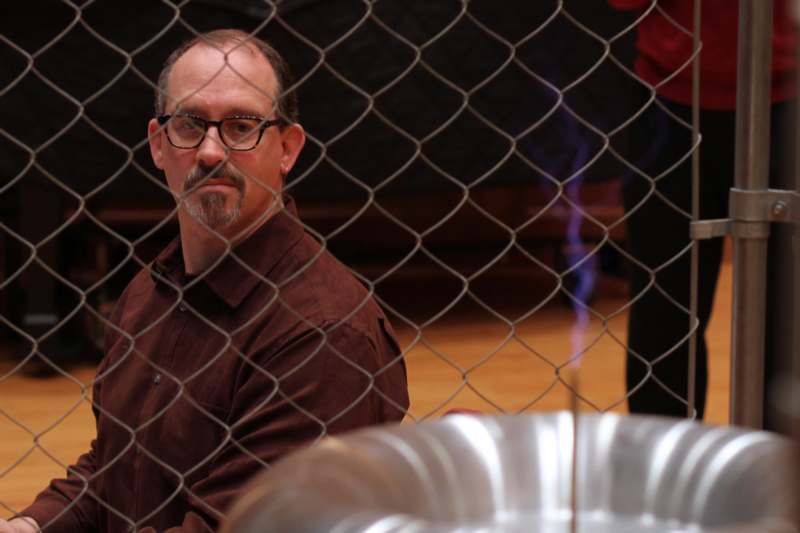 a man in glasses behind a chain link fence