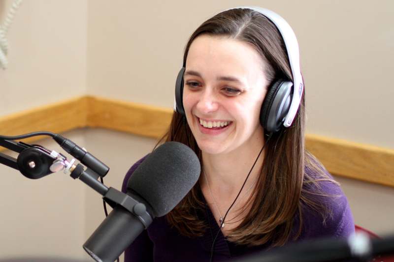 a woman wearing headphones and smiling at a microphone