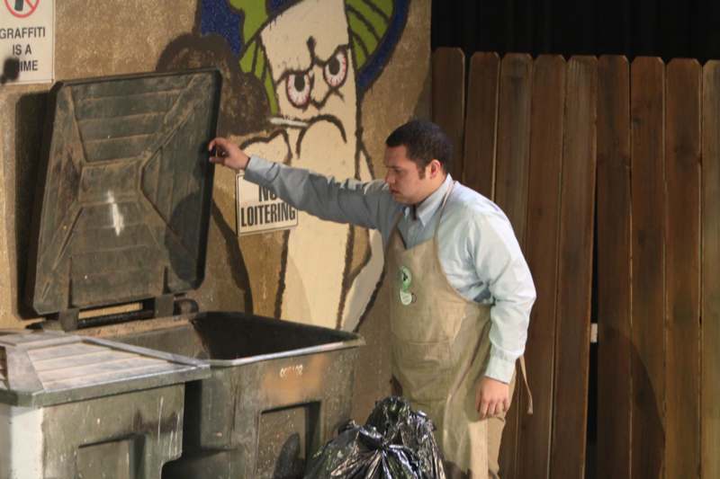 a man wearing an apron and standing next to a trash can