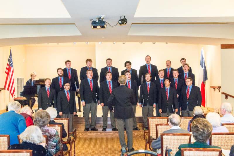 a group of men singing in a room with people watching