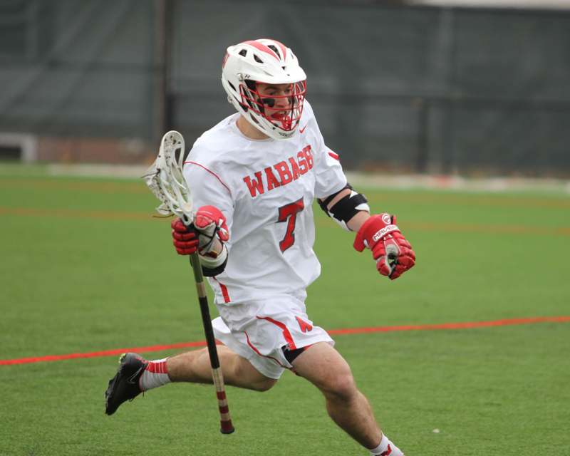 a man wearing a white and red uniform running with a lacrosse stick
