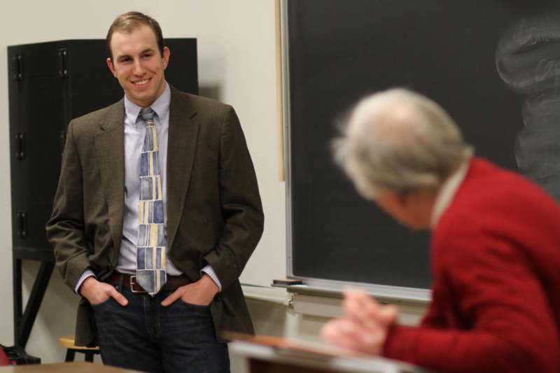 a man in a suit and tie standing in front of a man in a classroom