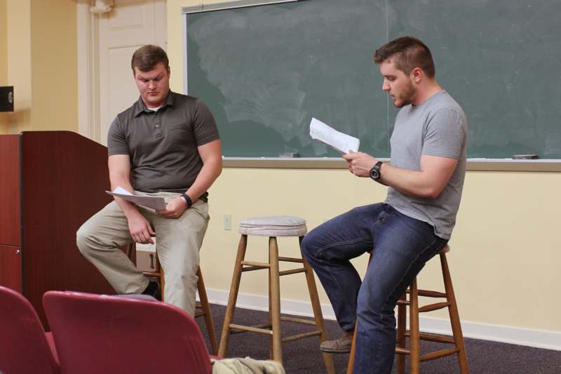 two men sitting on stools in a classroom