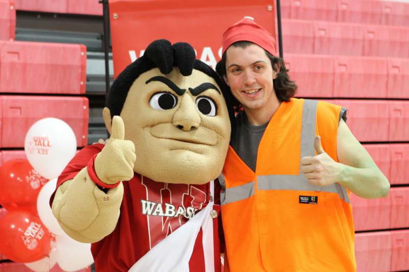 a man in a orange vest and a mascot posing with his thumbs up