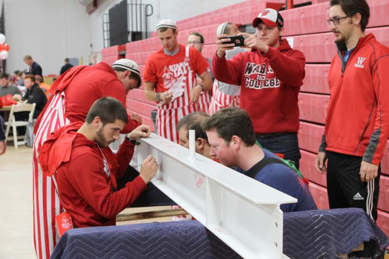 a group of men in red shirts working on a metal beam