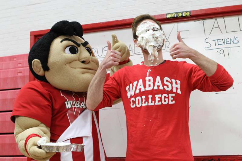 a man with a mascot and a cake on his face