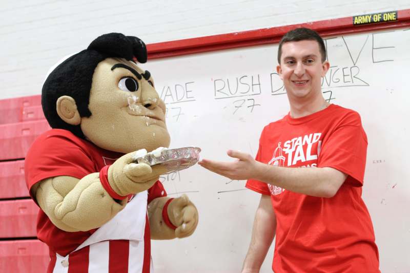 a man holding a plate of cake and a mascot