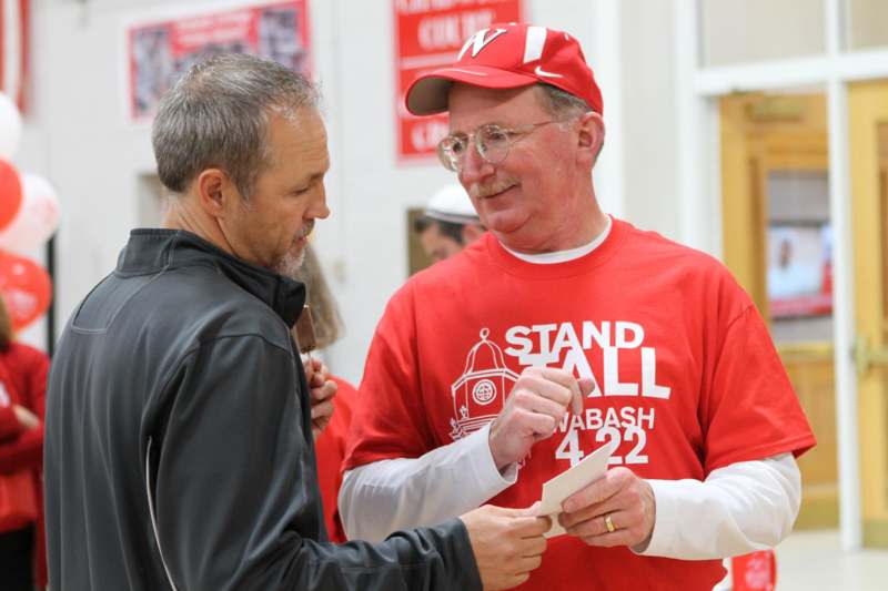 a man in red shirt giving a piece of paper to another man
