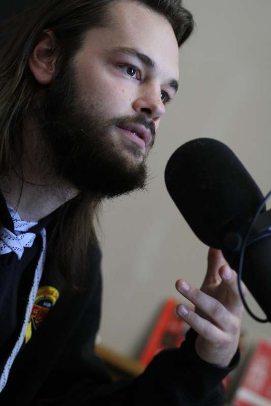 a man with long hair and beards speaking into a microphone