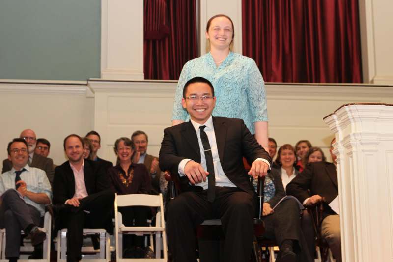 a man in a suit sitting on a chair with a woman standing behind him