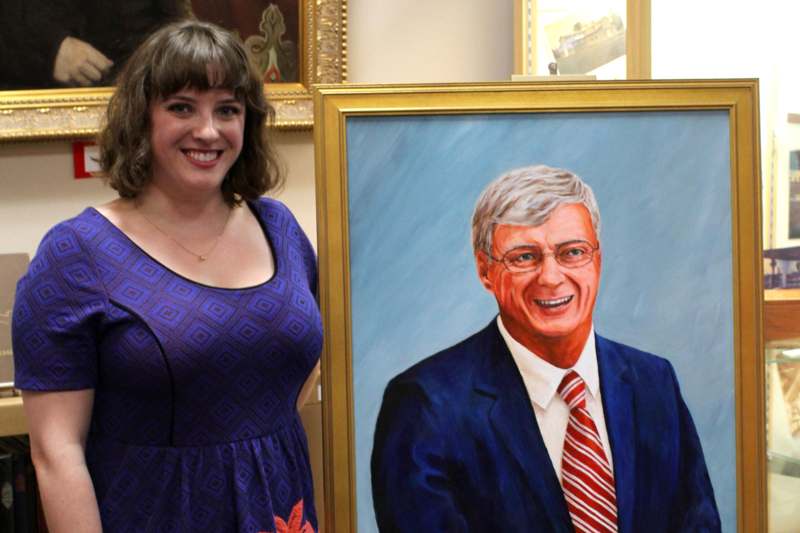 a woman standing next to a painting of a man