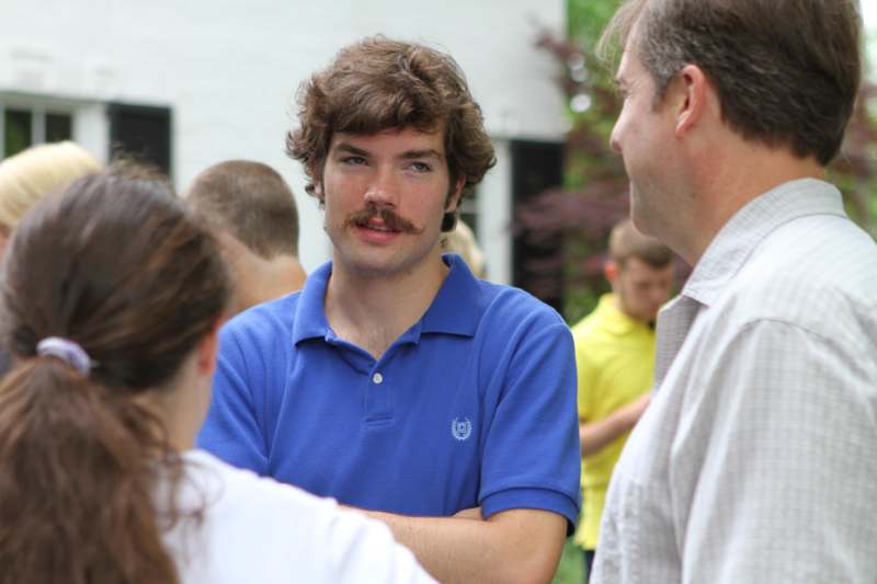 a man with a mustache and a blue shirt talking to a group of people