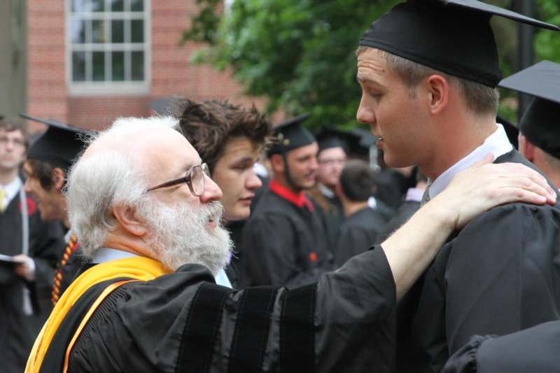 a man in a graduation cap and gown touching a man's neck