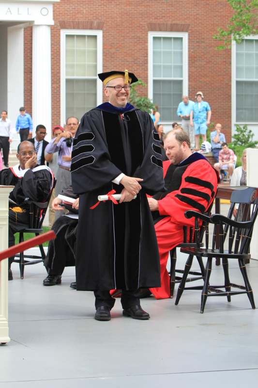 a man in a graduation gown shaking hands with another man in a red robe