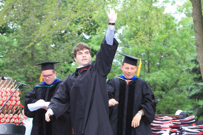 a group of people in graduation gowns and cap raising their hand