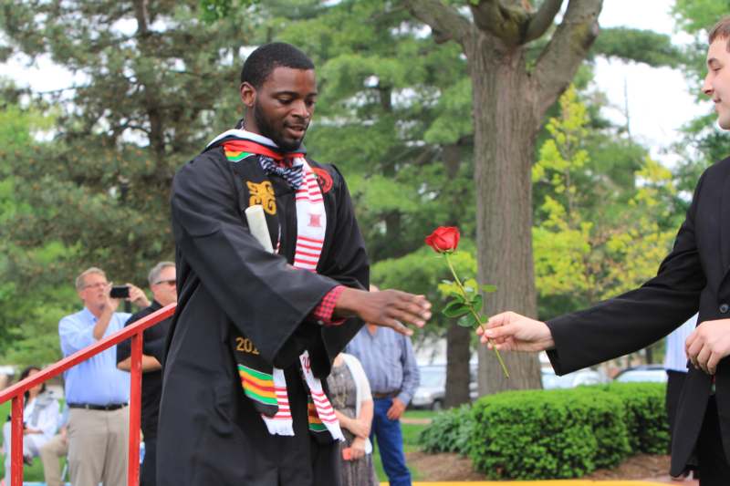 a man in a graduation gown receiving a rose from a woman