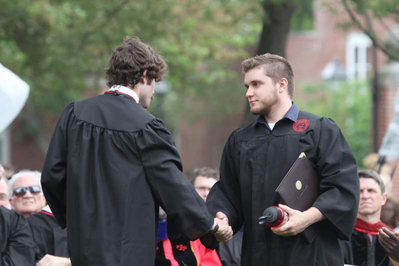 two men in graduation gowns shaking hands