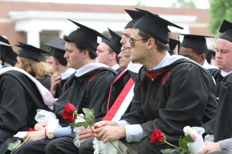 a group of people in graduation gowns and caps holding flowers