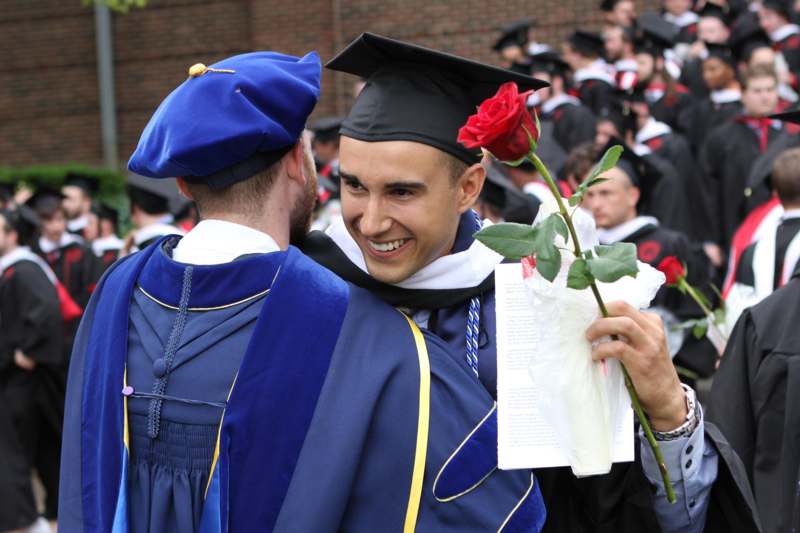 a man in graduation gowns holding a rose and smiling