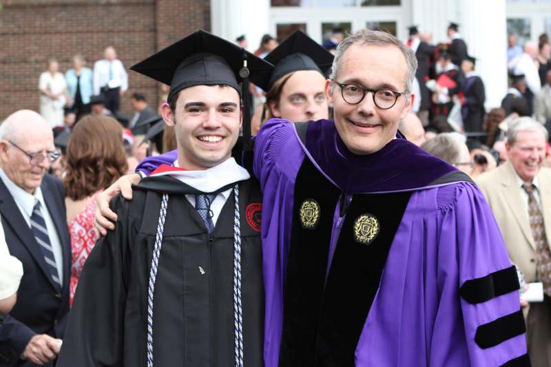 a man in a graduation gown and cap standing next to a man in a graduation gown