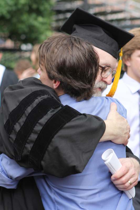 a man in a graduation gown hugging a man