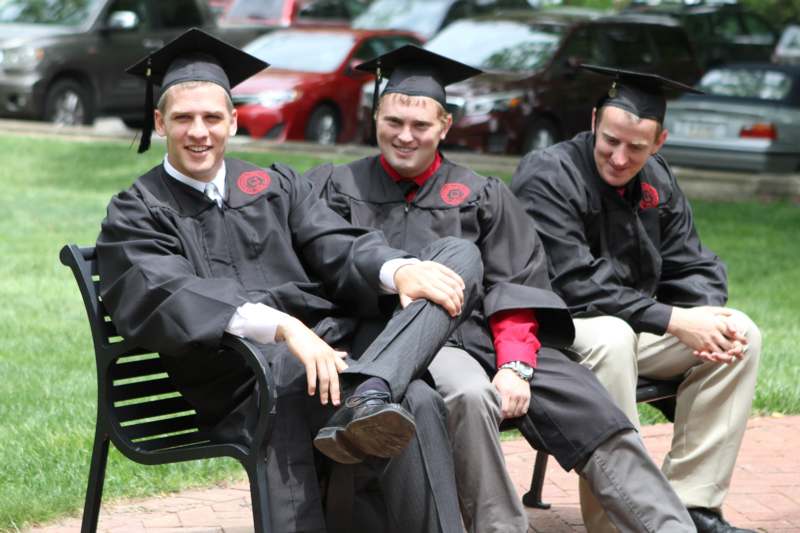 a group of men in graduation gowns and caps sitting on a bench